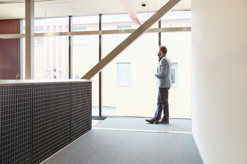 Geschäftsmann steht im Büro und schaut aus dem Fenster - RHF01964