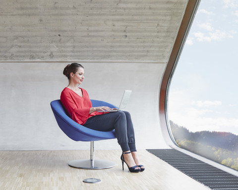 Woman sitting on chair in attic office using laptop stock photo