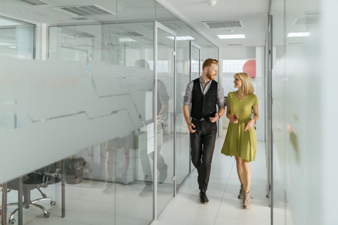 Geschäftsmann und Frau gehen im Bürokorridor und unterhalten sich, lizenzfreies Stockfoto