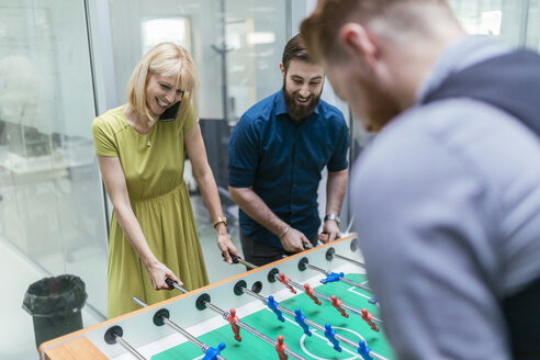 Colleagues playing foosball in office - ZEDF00647