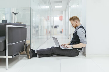 Businessman in office sitting on floor, using laptop - ZEDF00652