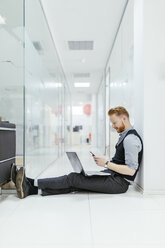 Geschäftsmann im Büro, der auf dem Boden sitzt und einen Laptop benutzt - ZEDF00653