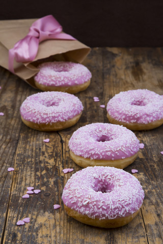 Krapfen mit rosa Zuckerguss und Zuckergranulat auf Holz, lizenzfreies Stockfoto