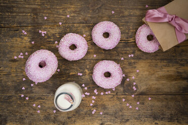 Doughnuts with pink icing and sugar granules and a bottle of milk on wood - LVF06174