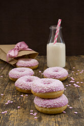 Doughnuts with pink icing and sugar granules and a bottle of milk on wood - LVF06175