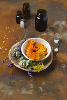 Blüten von Heilpflanzen, Medizinflaschen und Kügelchen auf rostigem Boden - MYF01933