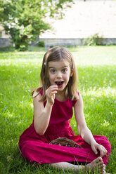 Porträt eines kleinen Mädchens im roten Sommerkleid, das auf einer Wiese sitzt und Kirschen isst - LVF06181