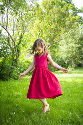 Little girl wearing red summer dress dancing on a meadow - LVF06182