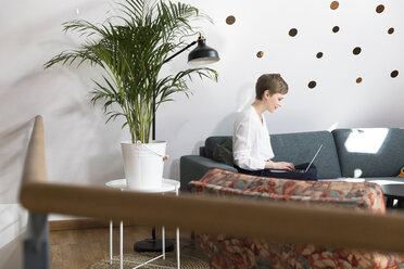 Frau benutzt Laptop auf Couch in modernem Büro - FKF02344