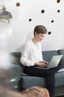 Frau benutzt Laptop auf Couch in modernem Büro - FKF02345