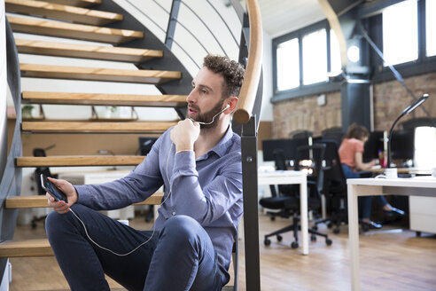 Mann in modernem Büro, der mit seinem Handy telefoniert - FKF02365