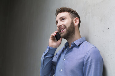 Smiling man on cell phone at concrete wall - FKF02399