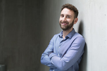 Portrait of smiling man leaning against concrete wall - FKF02403