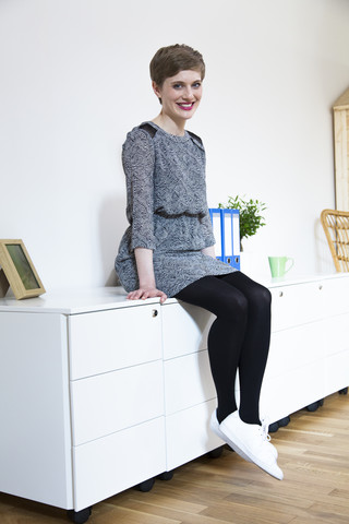 Lächelnde Frau sitzt auf einem Schrank im Büro, lizenzfreies Stockfoto