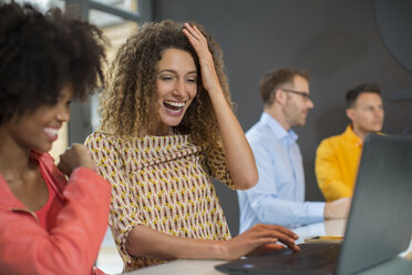 Zwei glückliche Frauen im Büro teilen sich einen Laptop - ZEF14016