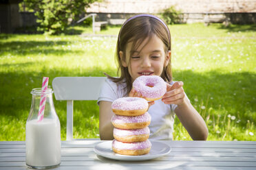 Mädchen mit Stapel von Donuts auf Gartentisch - LVF06190