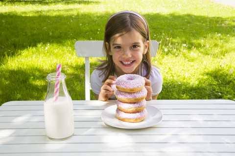 Glückliches Mädchen mit einem Stapel Donuts auf dem Gartentisch, lizenzfreies Stockfoto