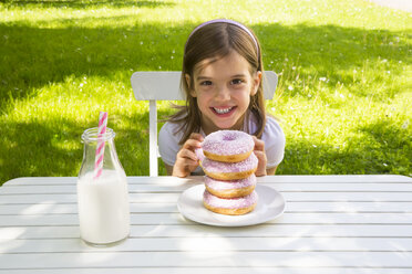 Happy girl with stack of donuts on garden table - LVF06191