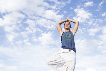 Woman doing a yoga exercise under sky with clouds - ABZF02128