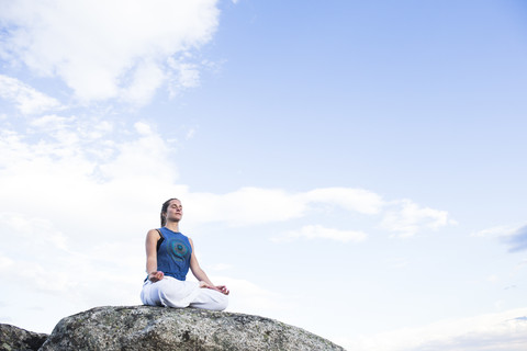 Frau beim Yoga auf einem Felsen sitzend, lizenzfreies Stockfoto