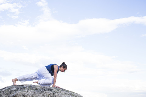 Frau bei einer Yoga-Übung auf einem Felsen, lizenzfreies Stockfoto