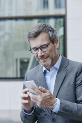 Lächelnder reifer Geschäftsmann, der ein Mobiltelefon benutzt - RORF00868