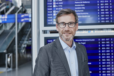 Lächelnder Geschäftsmann am Fahrplan auf dem Flughafen - RORF00895