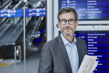 Lächelnder Geschäftsmann mit Zeitung am Fahrplan auf dem Flughafen - RORF00897