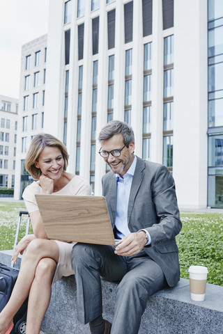 Happy businesswoman and businessman sharing laptop outdoors stock photo