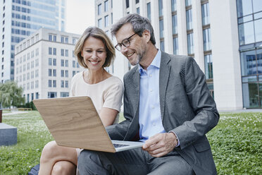 Smiling businesswoman and businessman sharing laptop outdoors - RORF00901