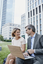 Smiling businesswoman and businessman sharing laptop outdoors - RORF00904