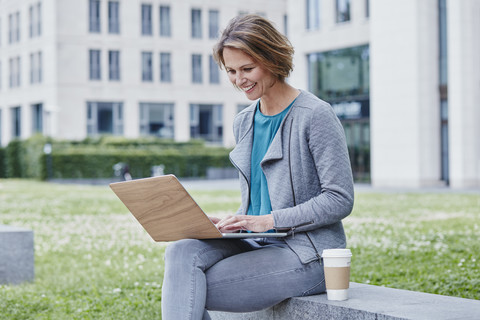 Happy woman outdoors with laptop and takeaway coffee stock photo