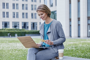 Woman outdoors with laptop, credit card and takeaway coffee - RORF00934