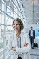Lächelnde Geschäftsfrau auf dem Flughafen, die aus dem Fenster schaut - RORF00948