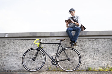 Geschäftsmann mit Fahrrad und Tablet an einer Wand - HAPF01726