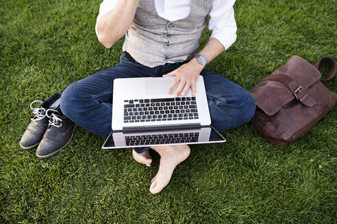 Unbekannter Geschäftsmann mit Laptop im Gras sitzend - HAPF01736