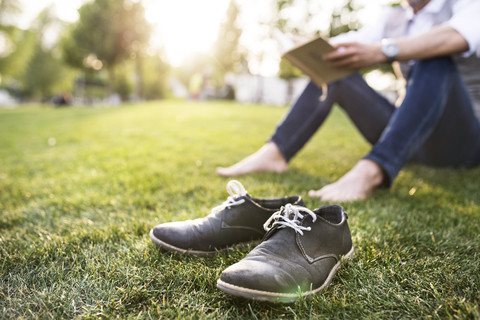 Unbekannter Geschäftsmann im Stadtpark, der im Gras sitzt und ein Buch liest, lizenzfreies Stockfoto