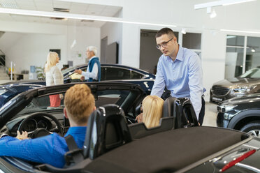 Salesman advising customers in car dealership - ZEDF00685