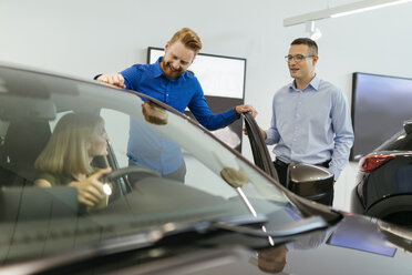 Salesman advising customers in car dealership - ZEDF00686