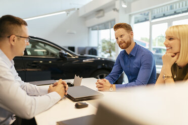 Salesperson advising couple in car dealership - ZEDF00705