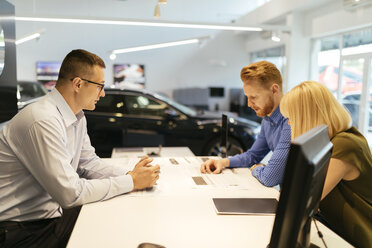 Salesperson advising couple in car dealership - ZEDF00706