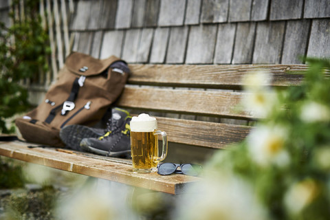 Deutschland, Bayern, Glas Bier, Rucksack, Sonnenbrille und Wanderschuhe auf Holzbank, lizenzfreies Stockfoto