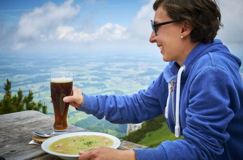 Deutschland, Chiemgau, glücklicher Wanderer auf dem Hochfelln mit einem Glas Bier und einem Teller Erbsensuppe - DIKF00252
