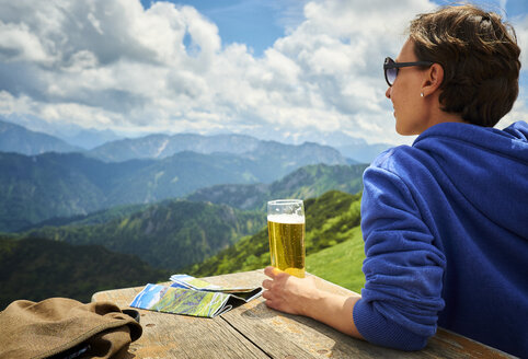 Deutschland, Chiemgau, Wanderer auf dem Hochfelln mit einem Glas Bier und Blick auf die Aussicht - DIKF00254