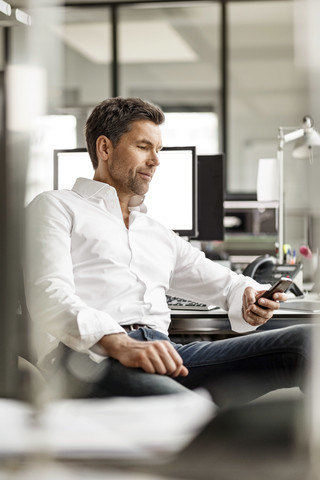 Geschäftsmann am Schreibtisch im Büro, der ein Mobiltelefon benutzt, lizenzfreies Stockfoto