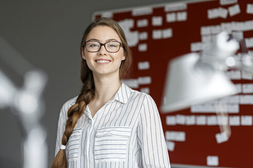 Porträt einer lächelnden jungen Frau in einem Büro vor einer Arbeitsplatte - PESF00721