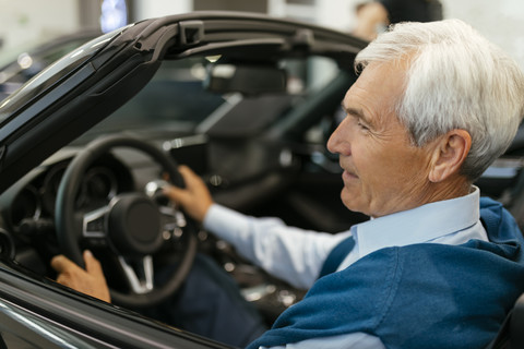 Älterer Mann testet Cabrio im Autohaus, lizenzfreies Stockfoto