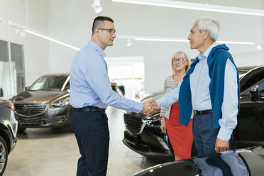Senior couple couple talking with salesperson in car dealership - ZEDF00723