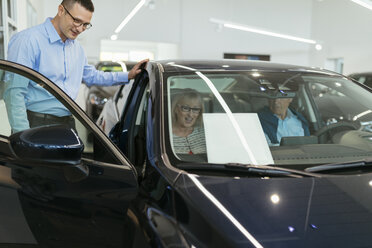 Salesman advising customers in car dealership - ZEDF00729
