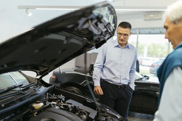 Salesman advising customer in car dealership - ZEDF00736